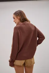 Sweater de tejido de punto color marrón chocolate, con cuello redondo y mangas largas con puños ajustados. Presenta un corte recto y holgado con el ruedo ligeramente asimétrico.