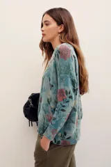 Sweater de punto con estampado floral en tonos rosados sobre base verde, cuello redondo y mangas largas.