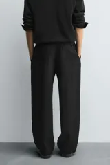 Pantalón negro de corte relajado con cintura elástica ajustable y pliegues en la parte delantera. Presenta bolsillos laterales y bolsillos traseros de parche.