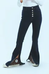 Pantalón de jean azul de tiro medio alto, corte oxford con botamanga ancha y tajo lateral. Cierre frontal con cinco botones metálicos.