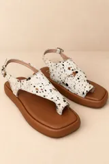 Sandalias planas de cuero vacuno con diseño tipo thong y tira ajustable en el talón. Capellada de cuero con pelo sintético en estampado animal print salpicado en tonos blanco, negro y marrón, sobre base marrón y suela plana.