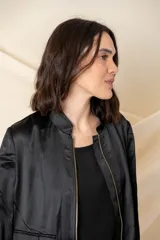 Campera tipo bomber color negro, confeccionada en tejido satinado. Presenta cierre frontal metálico, bolsillos laterales con hebillas decorativas doradas y puños elásticos.