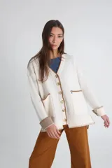 Cárdigan tejido color crudo con cuello en V, cierre con botones y bolsillos frontales con ribete en marrón.