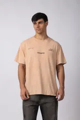 Remera de algodón con efecto de lavado gastado, color naranja suave. Presenta estampado frontal con texto y diseño minimalista, y corte holgado de estilo urbano.