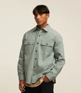 Camisa de manga larga confeccionada en sarga de algodón color verde menta, con cuello inglés y cierre frontal de botones negros. Presenta dos bolsillos de parche con solapa en el pecho y puños con botones.