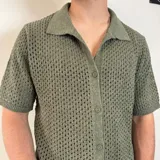 Camisa de tejido de punto calado en color beige, con cuello polo, cierre frontal de botones y mangas cortas.