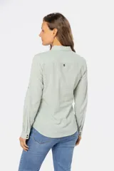 Camisa blanca de manga larga con cuello y tapeta de medio botón. Presenta dos bolsillos frontales con tapa y botones metálicos. Las mangas tienen presillas para sujetar el puño enrollado.