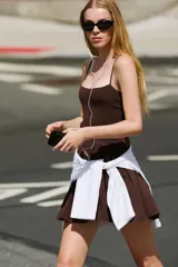 Vestido corto color marrón confeccionado en hilatura con mezcla de algodón, con escote redondo, tirantes finos y falda de vuelo con pliegues.