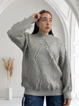 Sweater gris de tejido de punto con cuello redondo y mangas largas. Presenta un diseño con rombos y flecos.