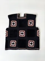 Chaleco sin mangas, confeccionado con cuadrados de cuero negro perforado combinados con cuadrados de crochet en hilo de algodón negro y blanco, con detalles centrales en rojo.