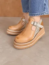 Guillerminas de cuero marrón chocolate, con detalles en animal print y textura dorada metalizada. Presentan una tira con hebilla metálica en el empeine, aberturas laterales y suela de plataforma corrida con franjas en contraste.