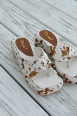 Sandalias con plataforma y capellada de cuero con estampado animal print de vaca en tonos marrón y blanco.