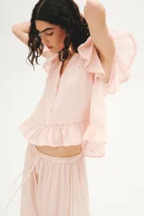 Blusa rosada de tejido liviano con alforzas e inserciones de encaje, escote en V pronunciado, cierre frontal de botones y mangas mariposa cortas con terminación fruncida en el ruedo.