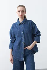 Sobrecamisa de jean azul de silueta relajada, con tachas aplicadas en líneas orgánicas. Tiene cuello camisero, cierre frontal con botones y mangas largas.