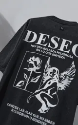 Remera de algodón premium con efecto nevado, corte oversize y cuello redondo. Presenta una estampa gráfica en color blanco en la espalda que incluye la palabra 'DESEO', una ilustración de una rosa y una figura alada, junto con frases poéticas.