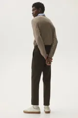 Pantalón de vestir color marrón oscuro, corte slim fit, con pliegue marcado en la pierna y puños doblados. Presenta cierre frontal con botón y bolsillos laterales y traseros.