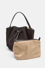Bolso de mano tipo saco mini, color marrón oscuro, con detalle de pespuntes en el cuerpo y cierre mediante botón imantado. Incluye tira ajustable frontal y compartimento interior con cremallera.