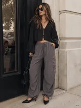 Pantalón cargo gris de corte ancho y relajado, confeccionado en tela fluida. Cuenta con cintura elástica con cordón de ajuste, bolsillos laterales, bolsillos cargo en las piernas y detalles de fruncido con cordones ajustables en los tobillos.
