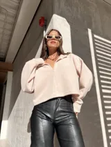 Buzo de cuello polo con escote en V, de corte holgado y diseño cropped. Presenta mangas largas con puños ajustados y una textura suave.