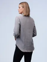 Camisa celeste de tencel con cuello con solapa, escote en V y abertura central con botones. Tiene bolsillos delanteros, mangas largas regulables con presilla y ruedo desflecado.