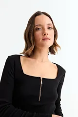 Remera de manga larga, color blanco, con tejido acanalado y escote cuadrado. Presenta un cierre metálico dorado en el centro del escote.