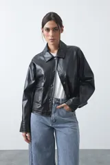 Chaqueta de cuero sintético negro con acabado brillante, cuello camisero, cierre frontal con botones a presión y bolsillos frontales con solapa.