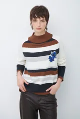Polera de tejido de punto con diseño de rayas horizontales en tonos beige, marrón, gris y negro. Presenta cuello redondo y mangas largas con puños en contraste.