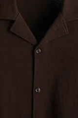Camisa de manga corta en punto jacquard color marrón, con cuello abierto y cierre frontal de botones.