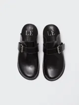 Zuecos de cuero color suela con diseño de punta redonda y ajuste mediante una tira con hebilla metálica en el empeine. Presentan una suela plana de goma negra y plantilla interior con logo grabado.