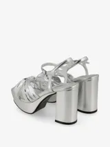 Sandalias de plataforma color plateado con diseño de tiras cruzadas anudadas en el empeine. Cuenta con taco cuadrado alto y cierre de pulsera con hebilla ajustable al tobillo.