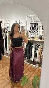 Pollera larga de satén bordó, estilo pareo con lazo lateral para ajustar en la cintura y delicado volado en el ruedo.