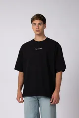 Remera negra de corte oversize con cuello redondo, mangas cortas y estampa pequeña con texto en el pecho.