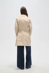 Trinchera de corte clásico, color negro, con cierre frontal de doble botonadura, solapas amplias y cinturón ajustable con hebilla en la cintura.