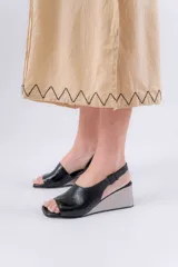 Sandalias negras de charol con punta descubierta, tira en el tobillo con hebilla y taco corrido plateado.