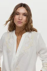 Camisa blanca de lino con cuello mao, manga larga y delicados bordados en tono tostado en el pecho y los puños.