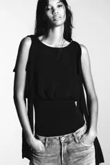 Body negro de cuello barco y tirantes con aplicación de lazos a tono. Cierre en bajo con botones a presión y en espalda con cremallera.