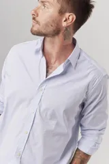 Camisa celeste a rayas verticales blancas, de corte clásico, manga larga y cuello abotonado.