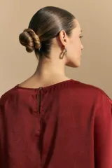 Top negro de manga corta con silueta amplia y caída fluida, confeccionado en un tejido liviano con leve brillo. Presenta un botón de nácar en la espalda con una pequeña abertura y mangas amplias tipo kimono.