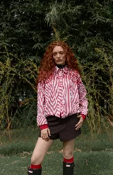 Camisa oversize de corte recto con estampado de rayas verticales en rojo y blanco. Presenta un diseño distintivo con bordados artesanales de mostacillas negras en la zona de los hombros y el canesú, cuello clásico y cierre frontal con botones.
