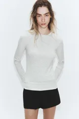 Camiseta de manga larga color gris melange, con cuello redondo y bajo recto. Presenta un detalle de tejido efecto doble a contraste en el cuello, puños y dobladillo inferior en color blanco.