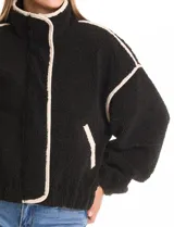 Campera negra de símil corderito, marca Elan. Tiene cuello alto, cierre frontal con solapa y botones, bolsillos inclinados en la parte delantera y ruedo y puños elastizados. Forro interno a tono.