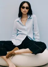 Camisa de lino celeste, de corte recto, con cuello camisero, cierre frontal de botones y mangas largas con puños abotonados.