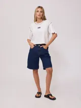 Remera blanca de algodón con corte cropped y calce holgado. Tiene cuello redondo con ribete azul y logo de la marca estampado en el pecho.