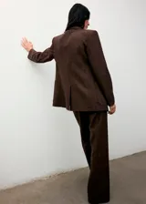 Blazer de corte recto confeccionado en tejido mezcla de lana con diseño jaspeado. Presenta cuello con solapas de muesca, cierre frontal con botones, dos bolsillos de parche delanteros, mangas largas con puños abotonados y abertura posterior en el bajo. Incluye forro interior.