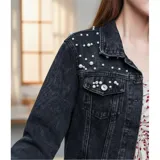 Campera de jean color negro con apliques de perlas en la parte superior frontal. Presenta cuello clásico, cierre frontal con botones metálicos y dos bolsillos en el pecho.