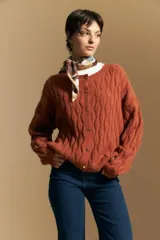 Cardigan de punto color terracota con diseño de trenzas verticales, cuello redondo y cierre frontal con botones metálicos. Presenta mangas largas con puños ajustados y un calce holgado.