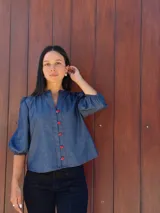 Camisa de jean azul con cuello mao, cierre frontal con botones rojos y mangas tres cuartos abullonadas con puños elásticos.