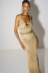 Vestido largo dorado de crochet con diseño artesanal y textura abierta, tirantes anchos y detalles de cordones cruzados en el escote y la cintura.