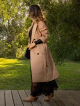 Trench color beige con doble botonadura, cuello clásico, solapas de muesca, cinturón y bolsillos laterales.