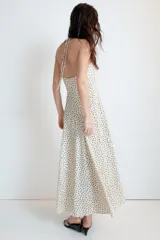 Vestido largo de color negro con cuello halter y escote recto. Presenta un diseño fluido con cierre de cremallera oculta en la espalda y lazada ajustable en el cuello.